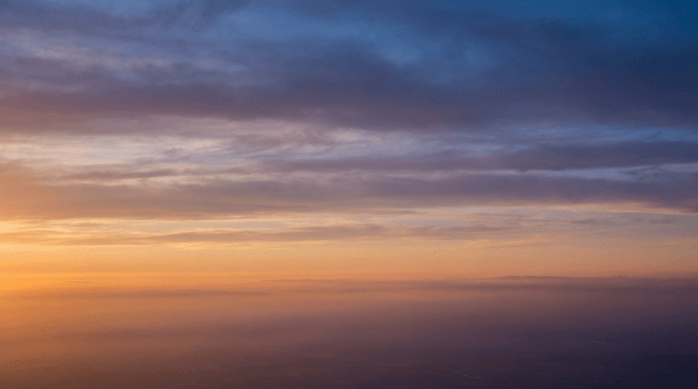 Expansive dusk cloudscape with golden horizon fading to cool blue sky, soft atmospheric haze, layered clouds.