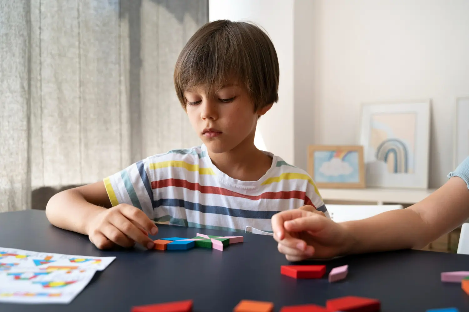A young boy concentrates while arranging colorful geometric wooden blocks on a dark table.